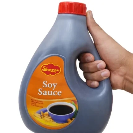 Shezan Soy Sauce large family-size bottle held in hand with grocery shelf background